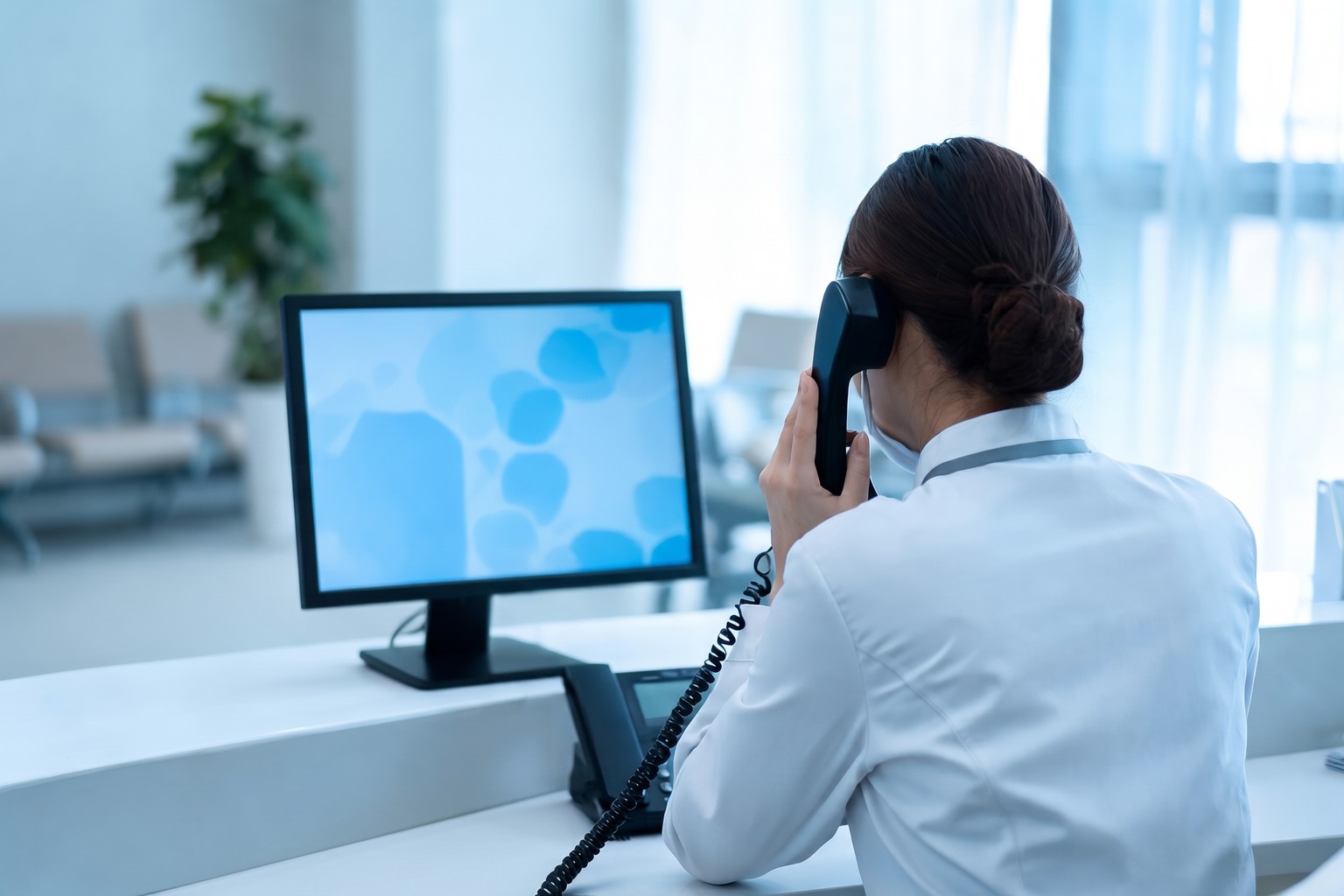 Healthcare administrator at a US clinic reception desk on a patient call handled with an Origins AI voice agent