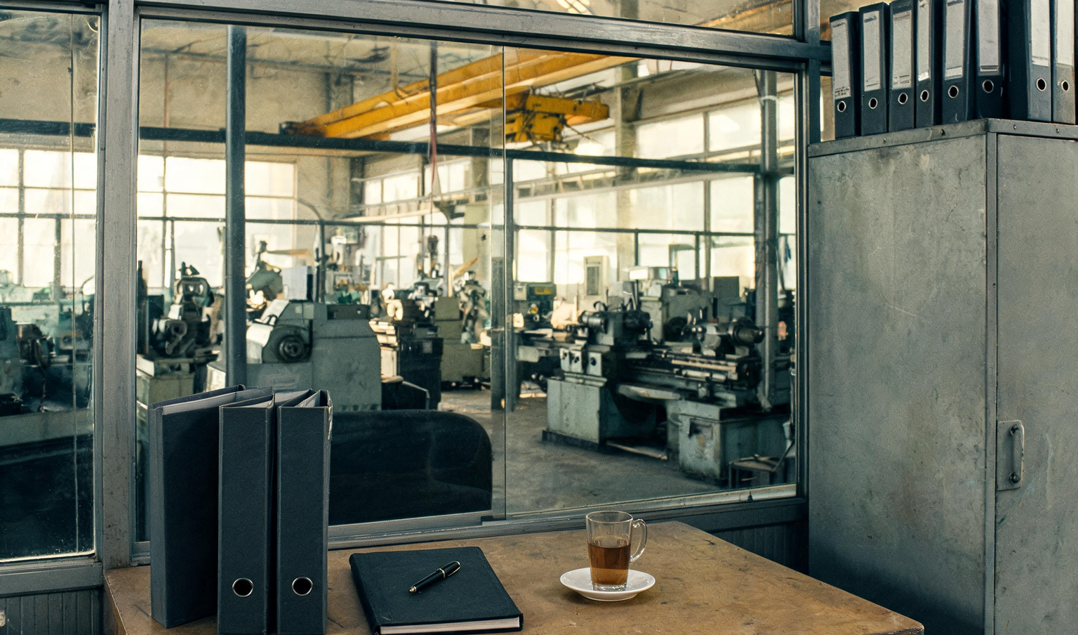 Finance cabin of a Coimbatore engineering unit with binders and a ledger on the desk, looking onto the machine shop